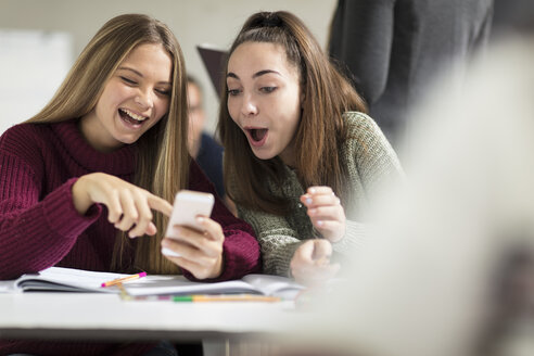 Glückliche Teenager-Mädchen in der Klasse, die auf ihr Mobiltelefon schauen - ZEF15665