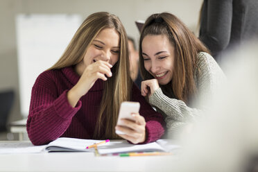 Glückliche Teenager-Mädchen in der Klasse, die auf ihr Mobiltelefon schauen - ZEF15666