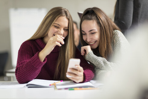 Glückliche Teenager-Mädchen in der Klasse, die auf ihr Mobiltelefon schauen - ZEF15666