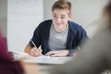 Smiling teenage boy taking notes in class - ZEF15668