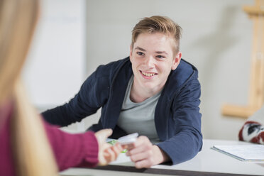 Smiling teenage boy passing a note to a girl in class - ZEF15671