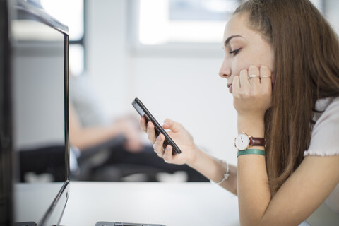 Teenager-Mädchen benutzt Handy im Computerunterricht, lizenzfreies Stockfoto