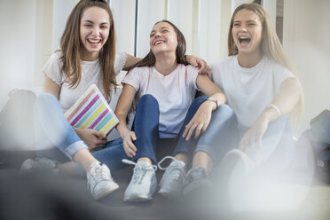 Glückliche Teenager-Mädchen sitzen auf dem Boden in der Schule - ZEF15723