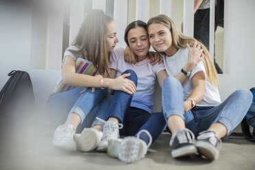 Smiling teenage girls sitting on floor in school hugging - ZEF15724