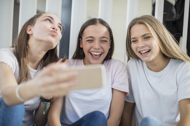 Happy teenage girls sharing cell phone in school - ZEF15725