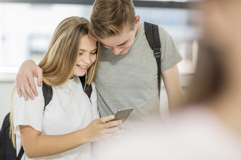 Junge umarmt Mädchen in der Schule und schaut gemeinsam auf sein Handy, lizenzfreies Stockfoto