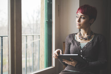 Young woman sitting by window, using digital tablet - CUF24486