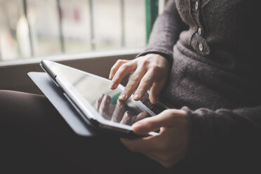 Junge Frau sitzt am Fenster und benutzt ein digitales Tablet, Fokus auf die Hände - CUF24487