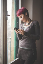 Junge Frau steht am Fenster und benutzt ihr Smartphone - CUF24489