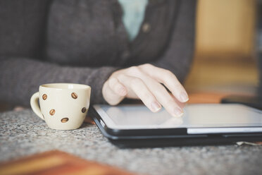 Young woman sitting at table using digital tablet, focus on hands - CUF24495