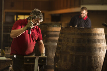 Männlicher Küfer bei der Arbeit mit dem Hammer in einer Küferei mit Whiskyfässern - CUF24505