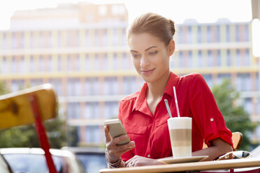 Young woman sitting outside cafe, using mobile phone - CUF24525