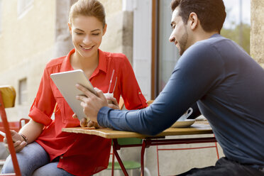 Young man and woman sitting outside cafe, looking at digital tablet - CUF24527