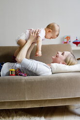 Mutter liegt auf dem Sofa und hält ihr kleines Mädchen in der Luft - CUF24550