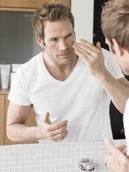 Mittlerer erwachsener Mann schaut in den Badezimmerspiegel und trägt Gesichtscreme auf - CUF24576