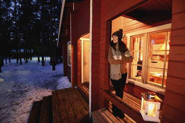 Porträt einer jungen Frau, die nachts aus einer Hüttenveranda schaut, Posio, Lappland, Finnland - CUF24601