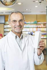 Portrait of senior male pharmacist holding up medicine in pharmacy - CUF24608