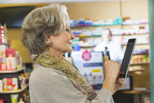 Eine ältere Frau benutzt ein digitales Tablet, um in einer Apotheke Medikamente online zu bestellen - CUF24609
