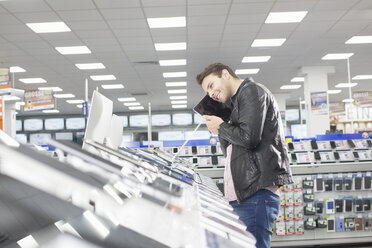 Young male shopper holding up chosen digital tablet in electronics store - CUF24615