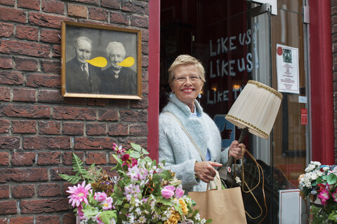 Ältere Kundin mit Lampe und Einkaufstasche vor einem Vintage-Laden, lizenzfreies Stockfoto