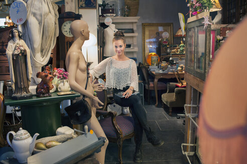 Porträt einer stilvollen jungen Frau, die in einem Vintage-Laden sitzt - CUF24651