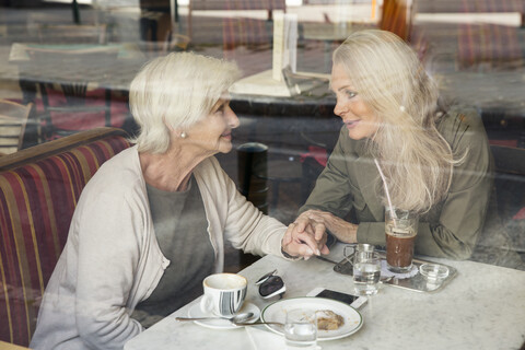 Mother and daughter sitting together in cafe, holding hands, seen through cafe window stock photo