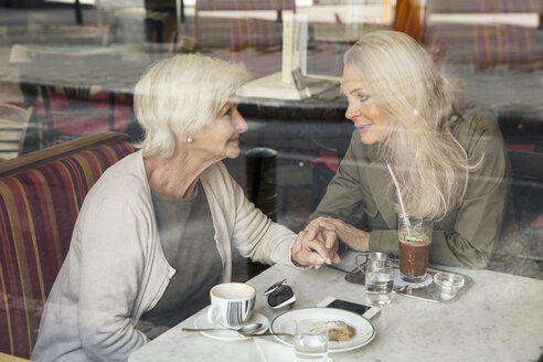 Mother and daughter sitting together in cafe, holding hands, seen through cafe window - CUF24661