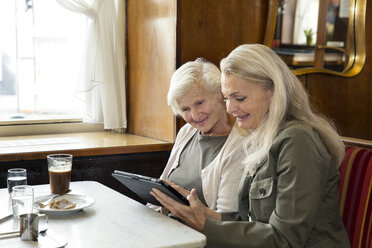 Mutter und Tochter sitzen zusammen in einem Café und schauen auf ein digitales Tablet - CUF24664