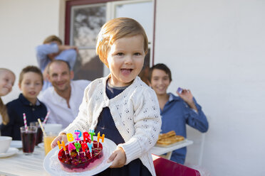 Female toddler carrying birthday cake on patio - CUF24689