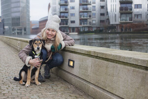 Porträt einer erwachsenen Frau und ihres Hundes am Flussufer der Stadt - CUF24690