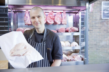 Portrait of butcher holding chicken breast in butchers shop - CUF24695