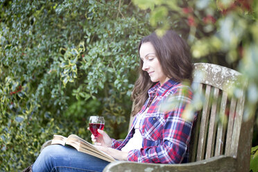 Mittlere erwachsene Frau liest auf einer Gartenbank in Thornbury Castle, South Gloucestershire, UK - CUF24705