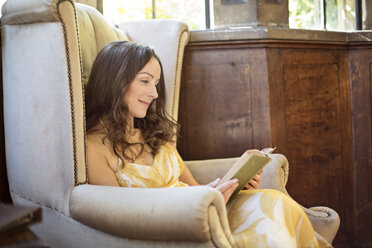 Woman reading book in old armchair at Thornbury Castle, South Gloucestershire, UK - CUF24707