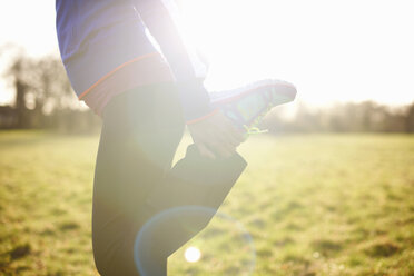 Ausschnitt einer reifen Läuferin, die ihr Bein in einem Feld ausstreckt - CUF24742