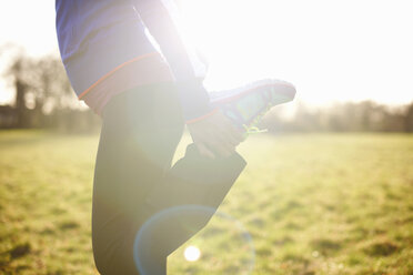 Cropped view of mature female runner stretching leg in field - CUF24742