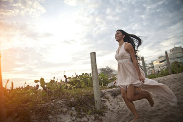 Mid adult woman running along sandy walkway towards beach - CUF24759