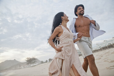 Mid adult couple running along beach, hand in hand, low angle view - CUF24765