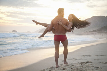 Mittleres erwachsenes Paar am Strand, Mann trägt Frau in den Armen, Rückansicht - CUF24771