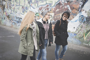 Drei Schwestern gehen an einer Graffiti-Wand vorbei - CUF24832