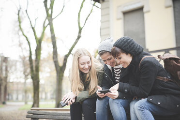 Drei Schwestern benutzen Smartphone auf einer Parkbank - CUF24845