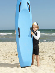 Porträt eines niedlichen Knirpses (Kindersurf-Rettungsschwimmer) neben einem Surfbrett am Strand, Altona, Melbourne, Australien - CUF24864