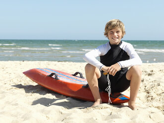 Porträt eines selbstbewussten kleinen Jungen (Kindersurf-Rettungsschwimmer) auf einem Surfbrett am Strand, Altona, Melbourne, Australien - CUF24867