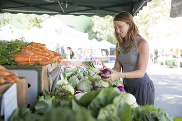 Woman at fruit and vegetable stall selecting red onions - ISF09377