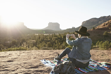 Frau sitzt auf einer Decke in der Wüste und fotografiert die Aussicht mit ihrem Smartphone, Sedona, Arizona, USA - ISF09391