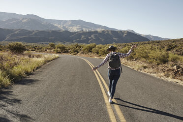 Woman walking along road markings of desert road, rear view, Sedona, Arizona, USA - ISF09395