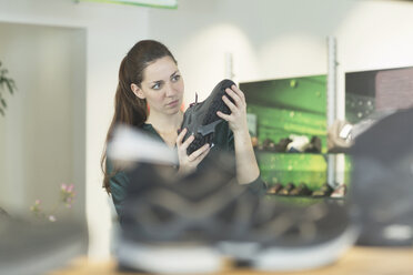 Junge weibliche Käuferin inspiziert einen Turnschuh in einem Schuhgeschäft - CUF25043