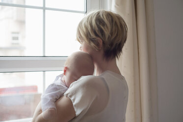 Mother carrying sleeping baby girl, looking out window - CUF25145