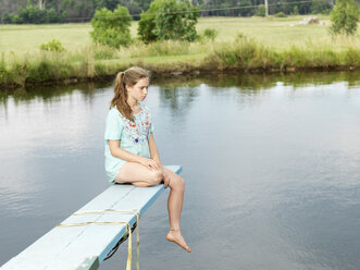 Teenage girl sitting on diving board over lake - CUF25157