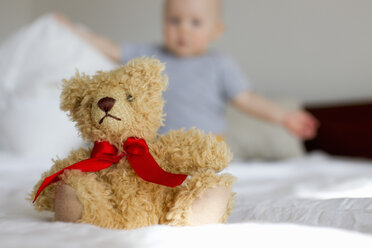 Cute teddy bear sitting up in bed in front of baby girl - CUF25259