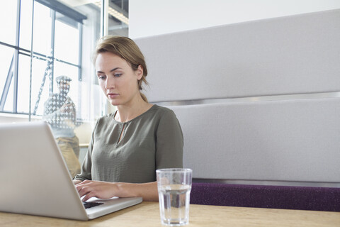 Junge Frau tippt auf einem Laptop im Büro, lizenzfreies Stockfoto